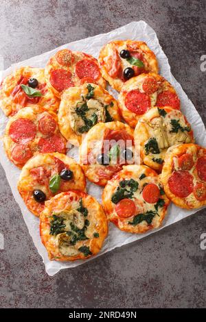 Hausgemachte Mini Pizzas Pizza mit fleischigen und vegetarischen Belägen aus der Nähe des Pergaments auf dem Tisch. Vertikale Draufsicht von oben Stockfoto