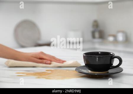 Eine Frau, die verschütteten Kaffee auf einem weißen Marmortisch in der Küche aufräumte. Platz für Text Stockfoto