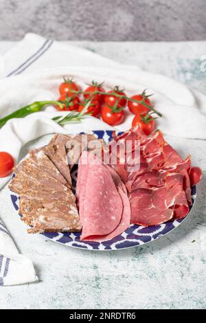 Kaltgeräucherter Fleischteller, Antipasto-Teller. Gebratenes Fleisch, Salami und Speck auf grauem Hintergrund Stockfoto