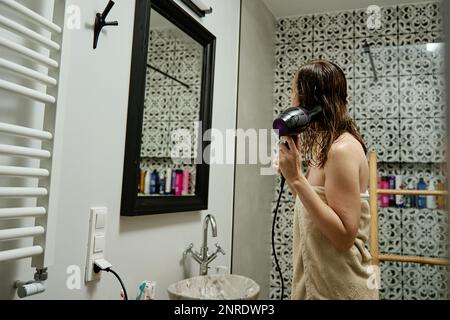 Frau in Handtuch eingehüllt, die Haare im Bad trocknet. Weibliche Morgenhygiene und Haarpflege Stockfoto