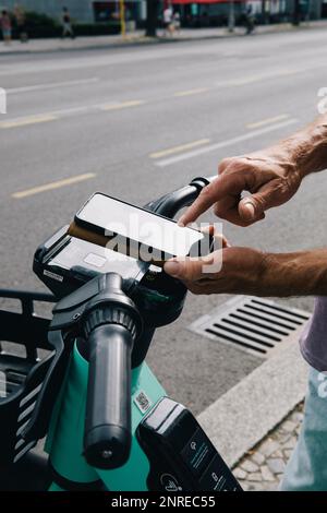 Nahaufnahme des elektrischen Schubrollers mit der Hand, der mit dem Smartphone entriegelt wird Stockfoto
