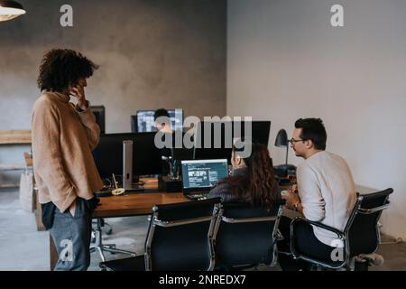 Geschäftsfrau, die mit männlichen und weiblichen Programmierern am Schreibtisch am Laptop arbeitet Stockfoto