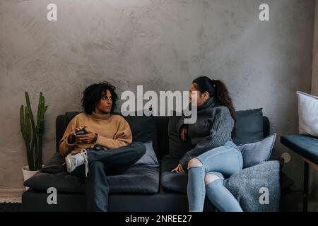 Geschäftsfrau, die mit einer Kollegin spricht, die in einer Startup-Firma auf dem Sofa sitzt Stockfoto