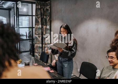 Glückliche Geschäftsfrau, die während des Meetings im Büro von männlichen und weiblichen Kollegen Tagebuch schreibt Stockfoto