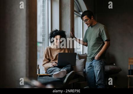 Lächelnde Geschäftsfrau, die ein Notebook von einem männlichen Kollegen im Kreativbüro benutzt Stockfoto