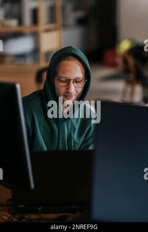 Junger männlicher Hacker, der in einer Startup-Firma an einem Laptop arbeitet Stockfoto
