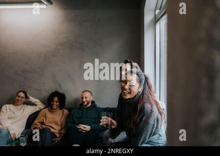 Fröhliche Geschäftsfrau, die Kaffee von Kollegen trinkt, während sie eine Pause in einem Startup-Unternehmen macht Stockfoto