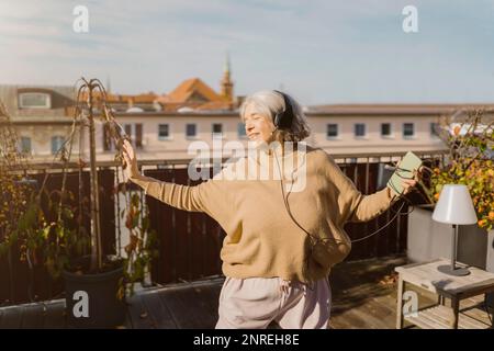 Sorgenfreie Seniorin, die Musik über Kopfhörer hört, während sie auf der Terrasse steht Stockfoto