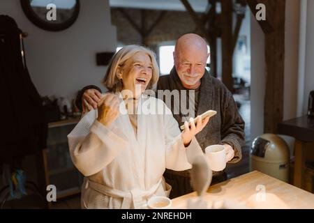 Eine ältere Frau, die lacht, während sie mit dem Mann zu Hause steht Stockfoto