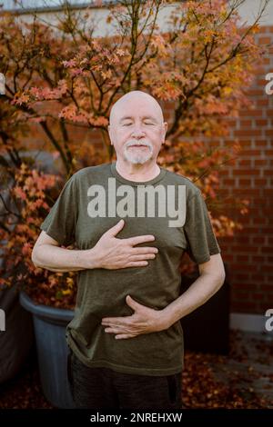 Seniorenmann, der Atemübungen macht, während er gegen die Pflanze steht Stockfoto