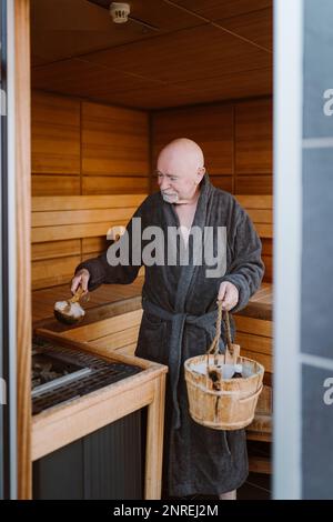 Ein älterer Mann, der in der Sauna heißes Stein in die Heizmaschine steckt Stockfoto