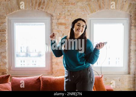 Fröhliche Frau tanzt, während sie zu Hause Musik hört Stockfoto