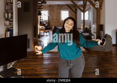 Frau tanzt im Wohnzimmer, während sie zu Hause Musik hört Stockfoto