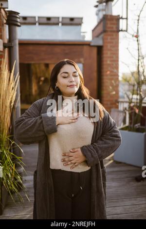 Frau mit geschlossenen Augen, die auf der Terrasse steht und Atemübungen durchführt Stockfoto