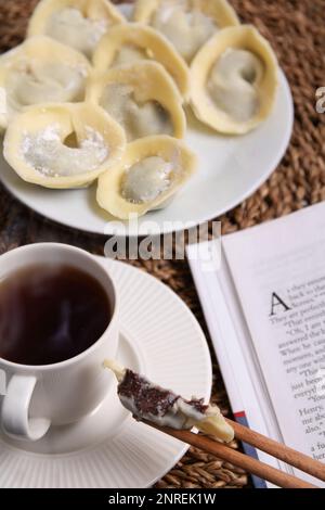 Fotos von vielen Schokoladensüßen in Form von weißen und dunklen Schokoladenknödeln liegen auf einem Teller neben einem Buch und einer Kaffeetasse, es gibt Dampf über t Stockfoto