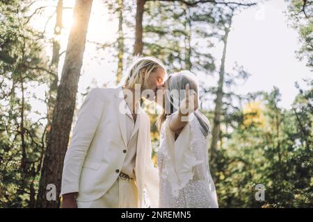 Die Braut zeigt Ringfinger beim Küssen des Bräutigams im Wald während der Hochzeit Stockfoto