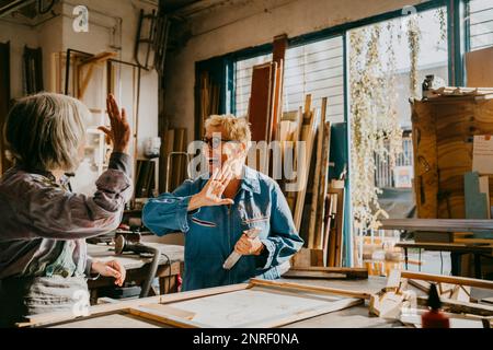 Fröhliche Handwerkerinnen, die High Five bei der Tischlerwerkstatt geben Stockfoto