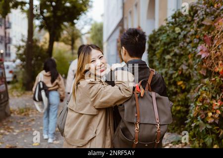 Porträt einer glücklichen Frau, die über die Schulter blickt, während sie mit einem männlichen Freund auf dem Bürgersteig läuft Stockfoto