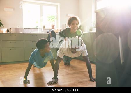 Vater macht Liegestütze, während er seinen Sohn zu Hause in der Küche trägt Stockfoto