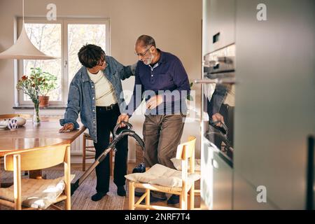 Seniorin, die mit einem Mann spricht, der sein Haus mit einem Staubsauger putzt Stockfoto