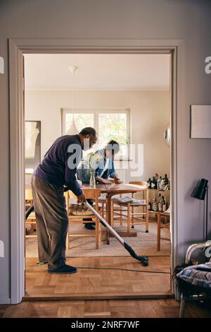 Seitenansicht eines Seniorenmanns, der mit Staubsauger durch die Haustür zu Hause sieht Stockfoto