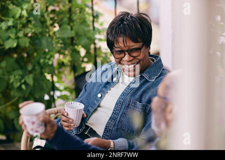 Glückliche Seniorin in Jeansjacke, die mit dem Mann einen Drink genießt Stockfoto