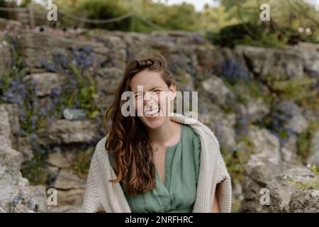 Ein Mädchen, das im Frühling in grünem Kleid in einem englischen Garten lacht Stockfoto