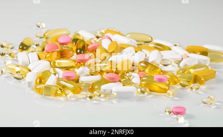 Mehrfarbige Pillen- und Kapselhaufen mit Bioadditiven mit Reflexion auf Glashintergrund. Stockfoto