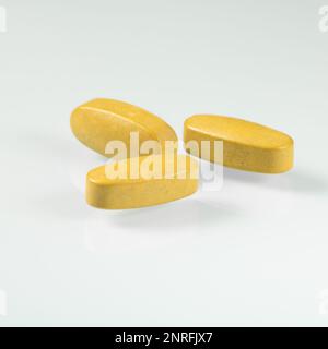 Drei große gelbe Tabletten mit Nahrungsergänzungsmitteln für Senioren aus der Nahaufnahme. Stockfoto