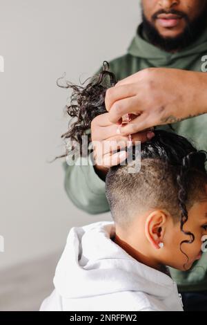 Nahaufnahme von schwarzem Dad, der birassistische Sohnes Haare in den Pferdeschwanz steckt Stockfoto