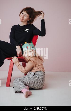Eine Frau in einem schwarzen Kleid sitzt auf einem Stuhl und hält die Hand eines Mädchens Stockfoto