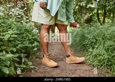 Aufnahme einer schwarzen Frau, die Beine spuckt, mit Insektenschutzmittel, das im Gras steht und in der Natur reist Stockfoto