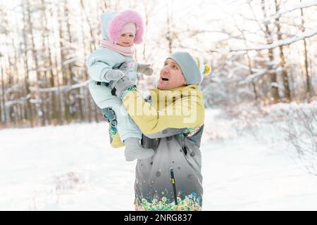 Vater und eine einjährige Tochter machen einen Spaziergang in einem verschneiten Park Stockfoto
