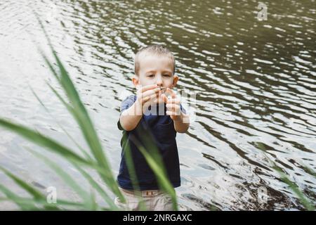 Porträt eines Jungen, der mit einer Muschel am Hintergrund des Flusses spielt Stockfoto