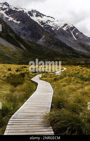 Eine Promenade im Freien führt in eine majestätische Berglandschaft mit schneebedeckten Gipfeln am Horizont Stockfoto