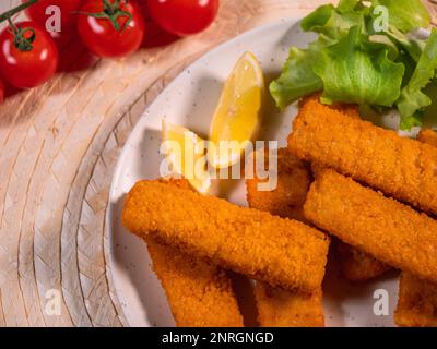 Fischstäbchen, leckere Meeresfrüchte, knusprig gebratene Fischfilets serviert mit Salat und Tomaten. Schnelles Fingerfood. Draufsicht. Stockfoto