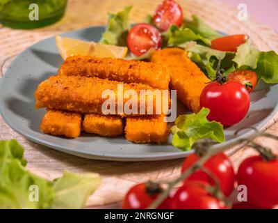 Fischstäbchen, leckere Meeresfrüchte, knusprig gebratene Fischfilets serviert mit Salat und Tomaten. Schnelles Fingerfood. Stockfoto