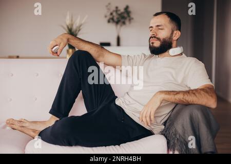 Der junge Mann benutzt ein Massagegerät für den Nacken, um sich zu Hause zu entspannen Stockfoto