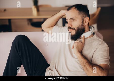 Der junge Mann benutzt ein Massagegerät für den Nacken, um sich zu Hause zu entspannen Stockfoto