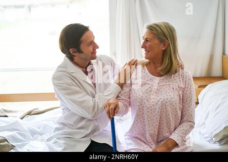 Lächelnder, fürsorglicher Arzt, umarmte Seniorin im Reha-Zentrum Stockfoto