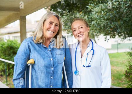 Porträt einer glücklichen Arztin im Garten mit einer behinderten Seniorin Stockfoto