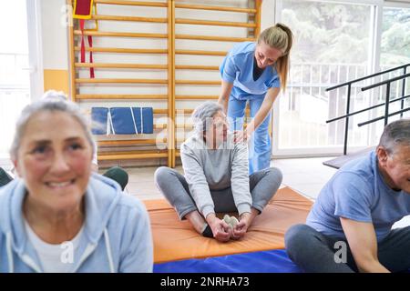 Lehrerin, die Seniorin beim Praktizieren der Kopfsteinpflasterhaltung im Rehabilitationszentrum unterstützt Stockfoto