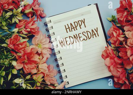 Happy Wednesday Typografie Text auf Papier Notizbuch flach auf blauem Hintergrund Stockfoto