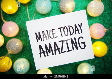 „Make Today Amazing“-Text auf einer Papierkarte mit LED-Baumwollkugeln auf grünem Hintergrund Stockfoto