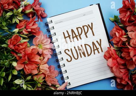 Fröhlicher Sonntag Typografie Text auf Papier Notizbuch flach auf blauem Hintergrund Stockfoto
