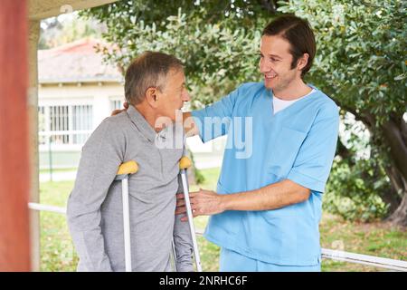 Lächelnde Krankenschwester unterstützt behinderten Senioren beim Gehen im Garten Stockfoto