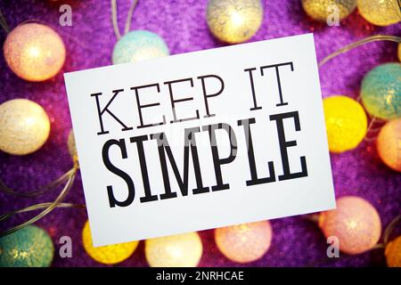 „Keep IT Simple“-Text auf Papierkarte mit LED-Baumwollkugeln auf lila Hintergrund Stockfoto