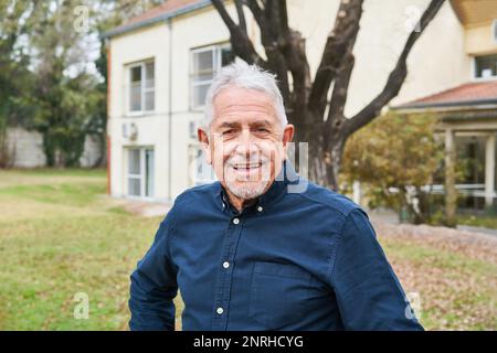 Porträt eines glücklichen älteren Mannes, der im Herbst im Garten des Pflegeheims steht Stockfoto