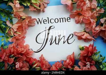 Begrüßungstext für Juni mit rosafarbenem Blumenrahmen auf blauem Hintergrund Stockfoto