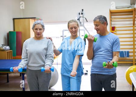 Krankenschwester, die Seniorenschwester und -Frau beim Training mit Kurzhanteln in der Reha-Klinik unterstützt Stockfoto